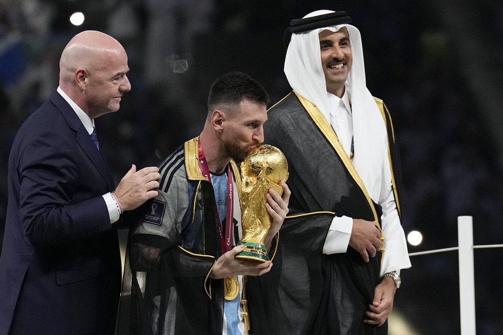 Na final da Copa de 2022, Messi beija a taça com traje entregue pelo emir Tamim bin Hamad bin Khalifa Al-Thani — Foto: Martin Meissner/AP